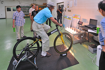 折りたたみ式でワンタッチで着脱可能な自転車発電機〈エネトレ〉は、別売りのインバーターを使用し自転車にセットすれば100Vの電源としてテレビを映すことも可能。
