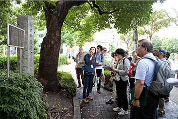 「浅野内匠頭邸跡」の石碑の前で馬場さんの説明に耳を傾ける参加者たち