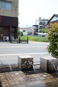 駅西通りの道路わきではポンプで汲みあげた地下水が放物線を描く