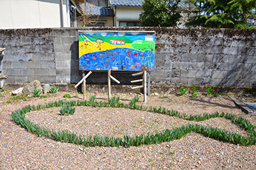 義景清水のそばにある「義景イトヨ保存会」のメンバーが草でかたどったイトヨの姿。奥にあるのは市内の小学生たちが書いた義景清水とイトヨの絵