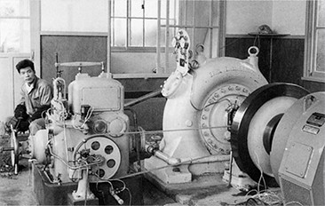 広島県の布野村農協・天神発電所（発電出力120kW）。左に写っているのは、若かりしころの沖さん。1960年（昭和35）。