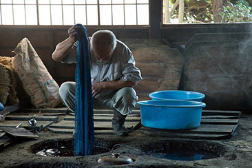 藍甕にゆっくり布を浸けて色を染めている職人の小島卓磨さん