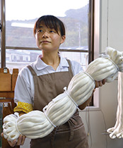 シルク博物館に隣接する「絹織物館」の製糸所で働く繰糸工（そうしこう）の井関奈央さん。手にするのは出荷前の「伊予生糸」