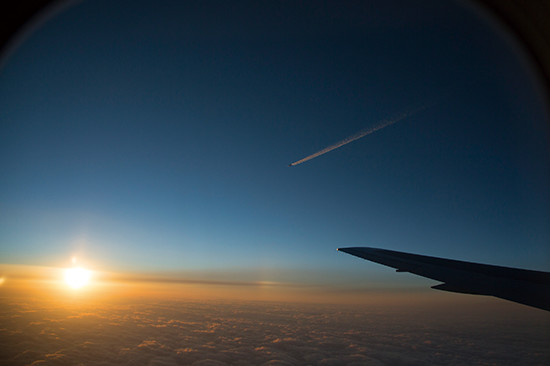 機中から見た雲海と夕日。向こうには別の旅客機と飛行機雲が見える