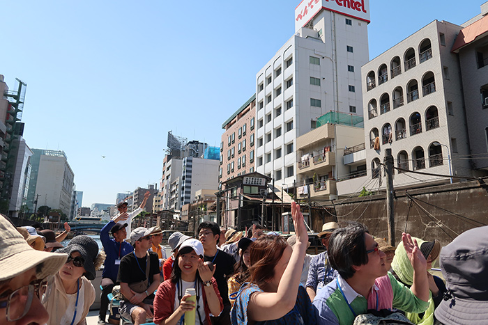 隅田川で地上にいる方に手を振る参加者　
クルーズ中、さまざまな場面で地上から川を覗く方たちと手を振り合いました