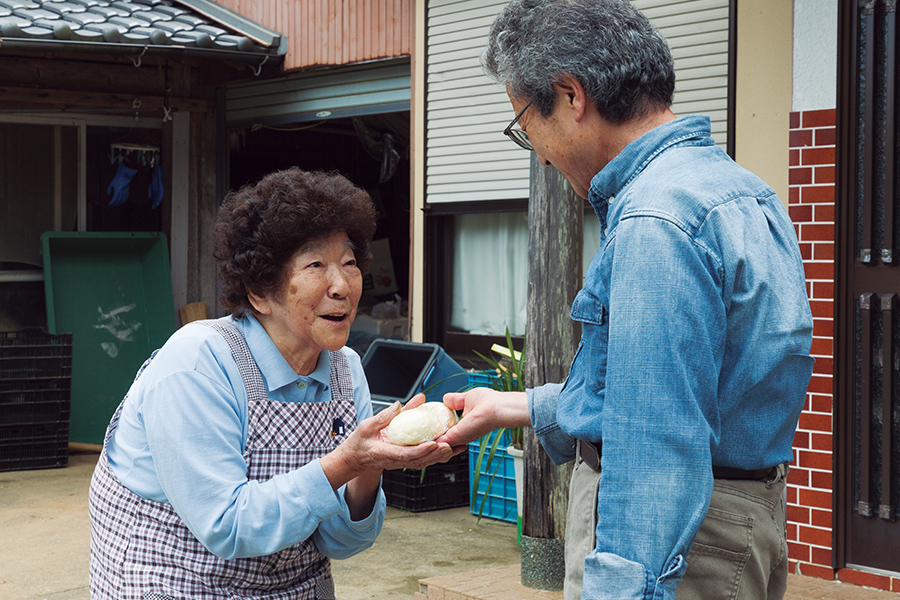 まんじゅうを手渡しで全戸に配る「念仏講まんじゅう」。山川河内地区で続けられている風習を自治会長の山口辰秋さん（右）と川端綾子さん（左）が再現