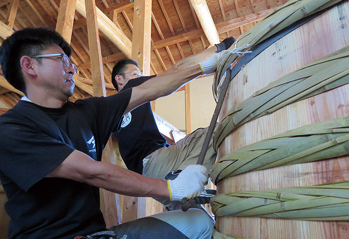 木桶づくりの作業風景。編んだ竹たがで側板を締め、底板にかんなをかけるなど数多くの工程がある。「木桶職人復活プロジェクト」には120名が加入し、毎年少しずつ増えている（提供：ヤマロク醤油株式会社）