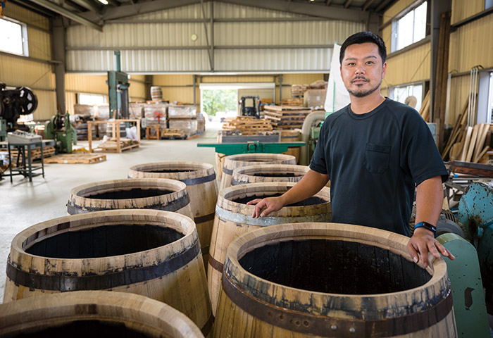 ミズナラの樽とクーパーの永江健太さん。永江さんは鹿児島の焼酎メーカーからの転身。自分たちの手で一から樽をつくれる今の環境は楽しいと話す