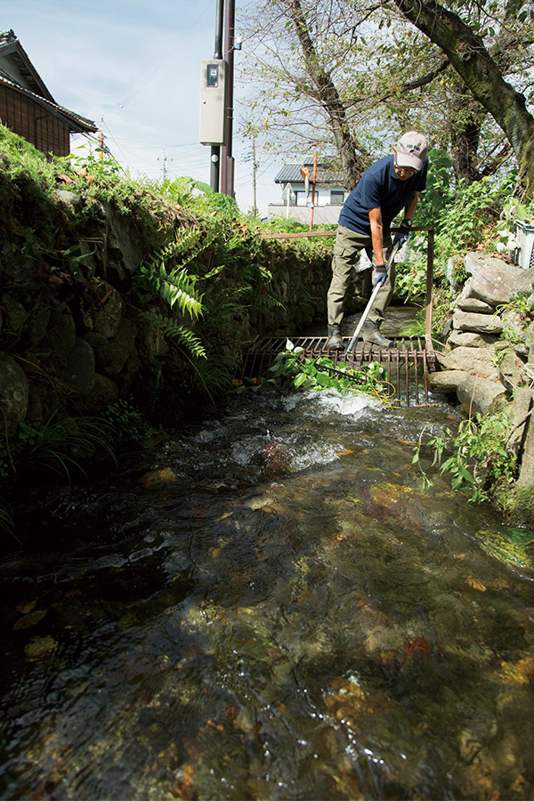 雄川堰を流れてきたごみを爪鍬（つめくわ）で引き上げる。住民が毎日この作業を行ない、清い流れを維持している