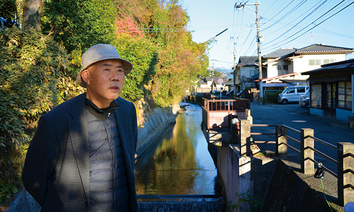 上井手（堀川）に架かる石造りの眼鏡橋で大津町の歴史について語る村下洋一さん。上井手沿いの通りが「塘町筋」で、旅籠や商家などが軒を連ねる宿駅大津の中心地だった