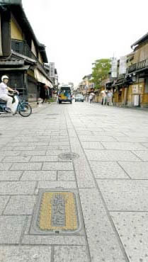 京都・祇園の花見小路通、新しく敷かれた石畳に、ファサードをそろえた町家が並ぶ。黄色く塗られた消火栓は抑えめの色合いで、蓋の文字も書き文字。